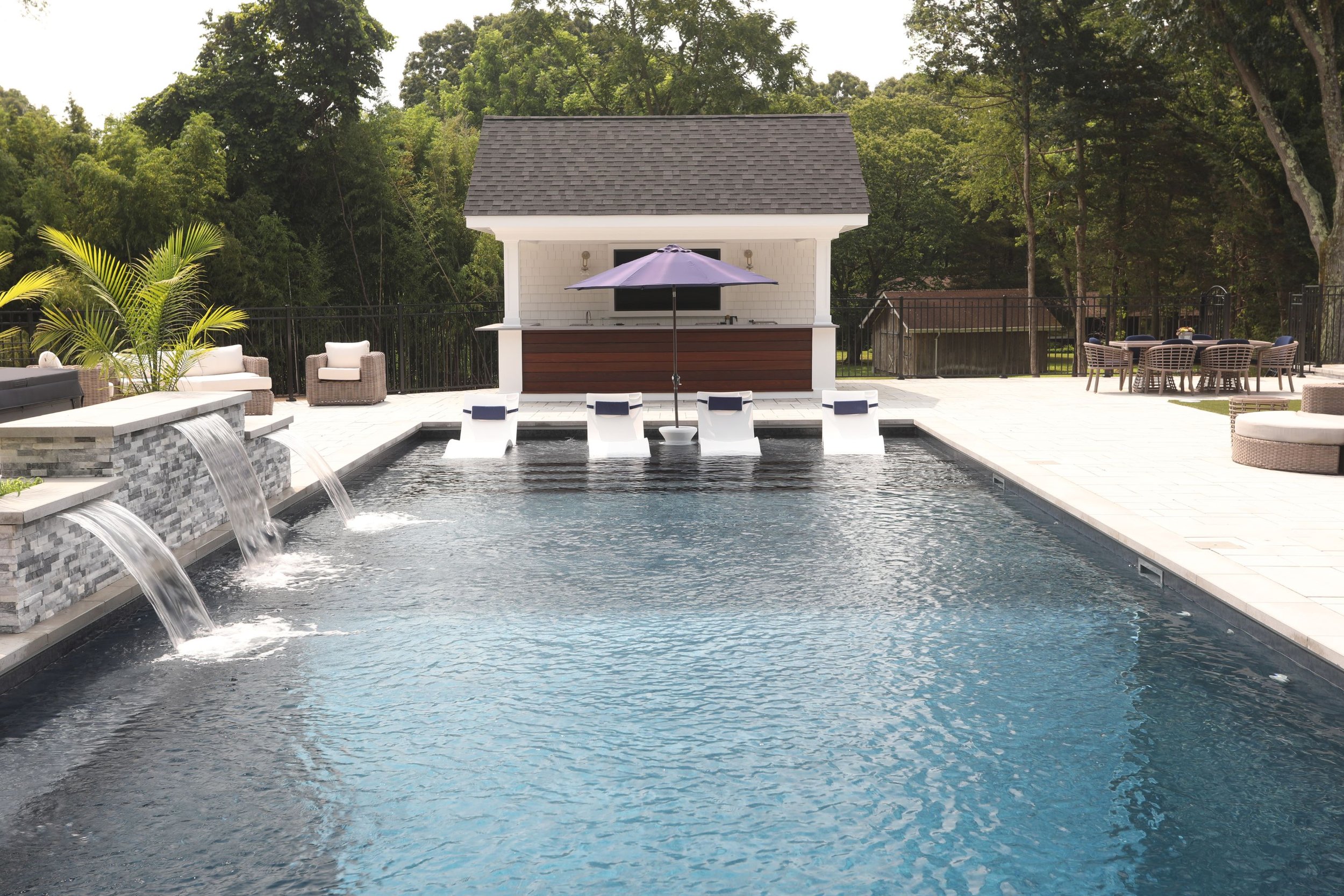 Dark-finish geometric pool with sheer descents, in-pool loungers and a private cabana